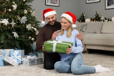 Happy couple in Santa hats with Christmas gift at home