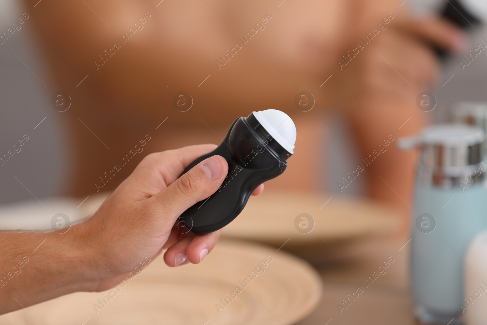 Photo of Young man holding deodorant in bathroom, closeup