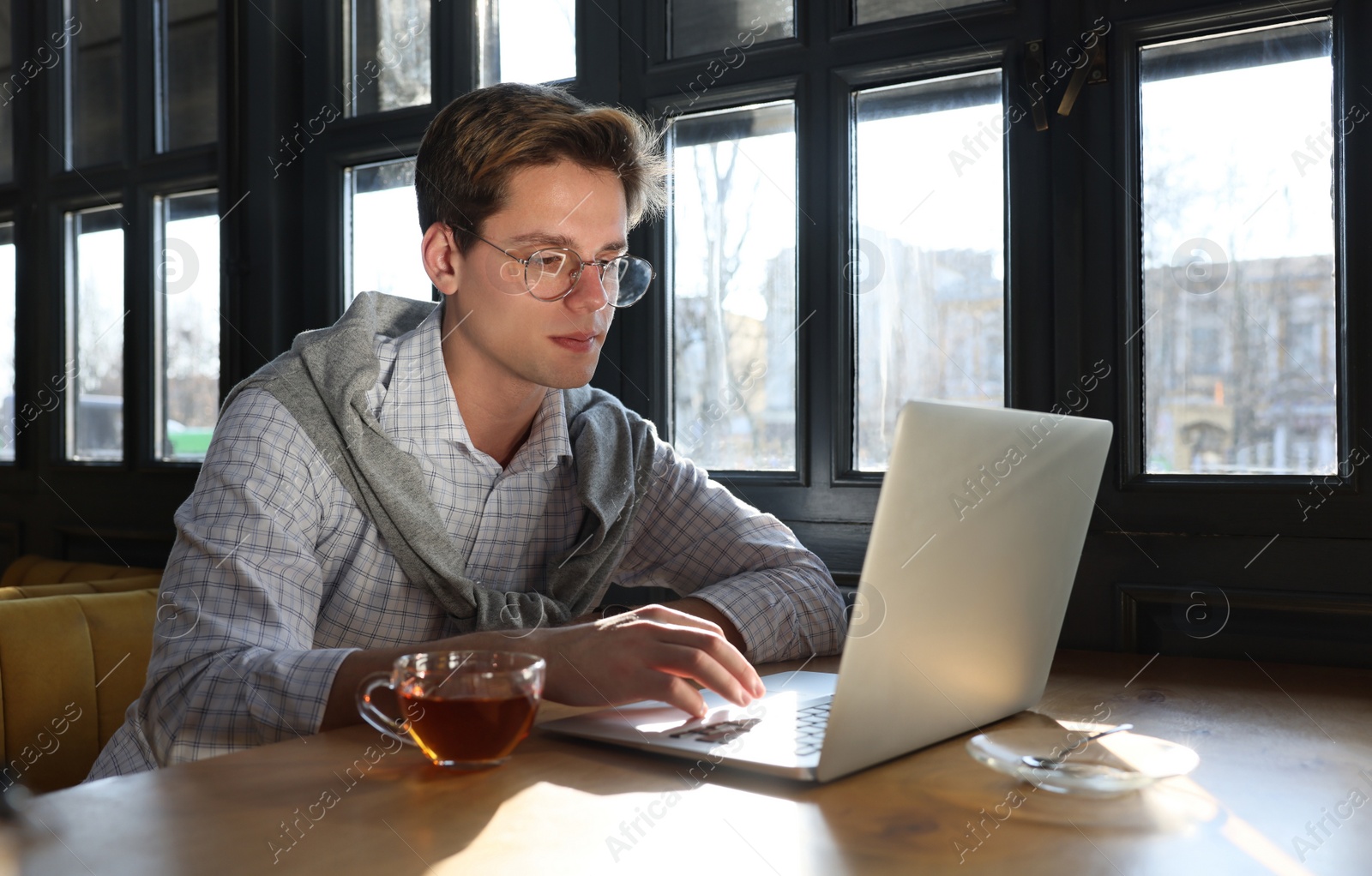 Photo of Teenage student with laptop studying at table in cafe