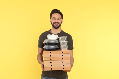 Young courier with different orders on color background. Food delivery service