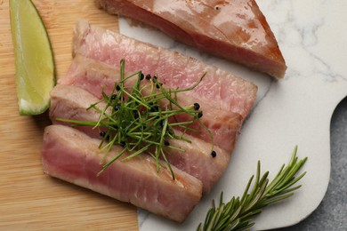 Photo of Pieces of delicious tuna steak with microgreens, lime and rosemary on table, top view