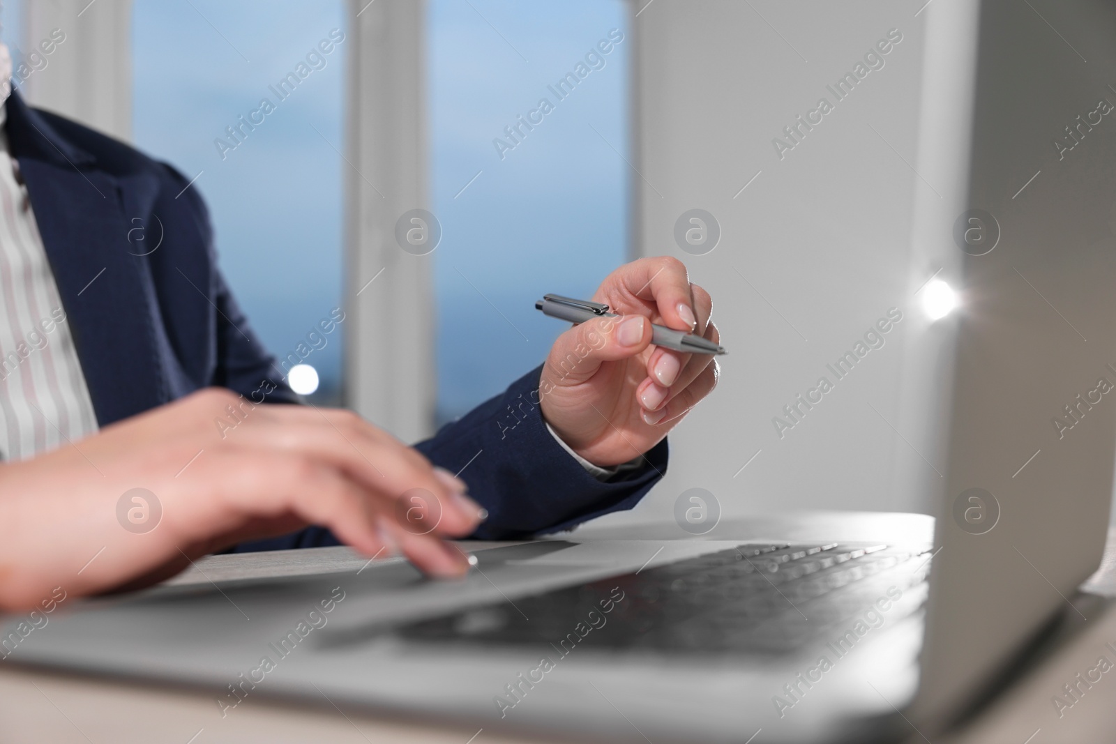 Photo of Woman with pen working on laptop at wooden table, closeup. Electronic document management