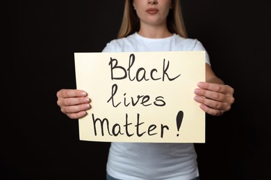 Young woman holding sign with phrase Black Lives Matter on dark background, closeup. Racism concept