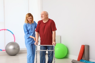 Photo of Caretaker helping elderly man with walking frame indoors