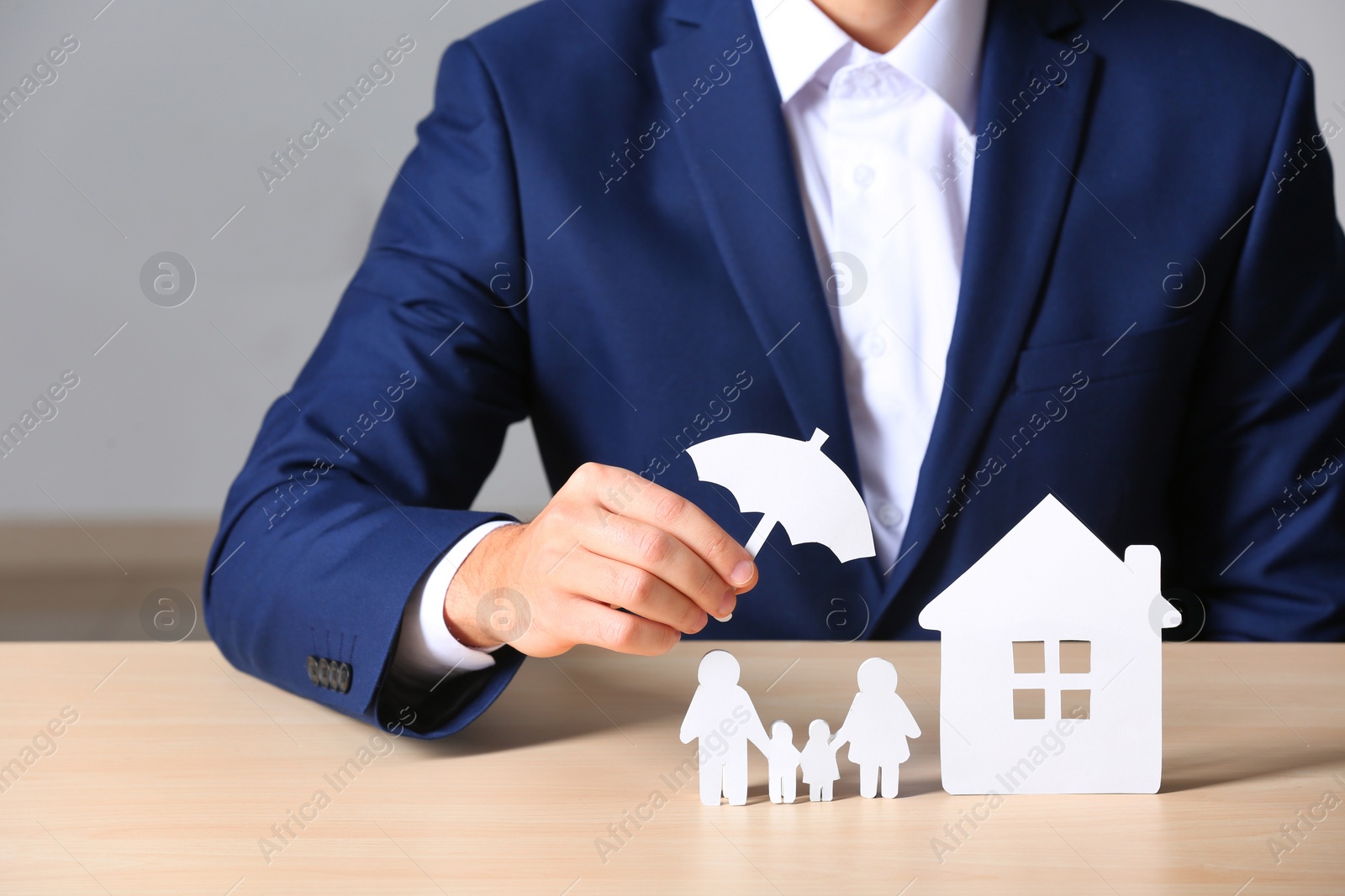 Photo of Male insurance agent covering paper family and home with umbrella cutout at table, closeup