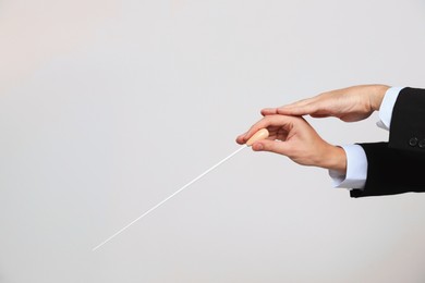 Professional conductor with baton on light grey background, closeup. Space for text