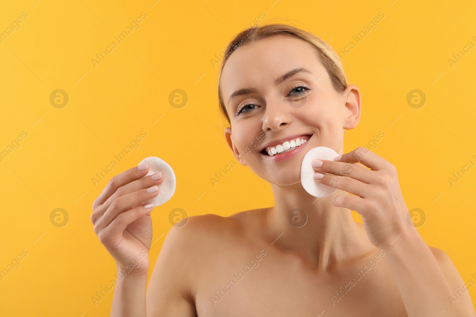 Photo of Smiling woman removing makeup with cotton pads on yellow background