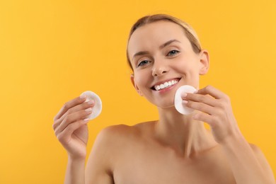 Smiling woman removing makeup with cotton pads on yellow background