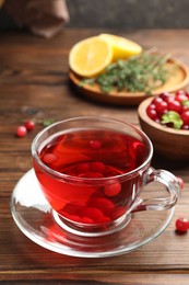 Photo of Tasty hot cranberry tea in glass cup and fresh berries on wooden table