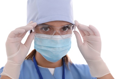 Doctor in medical gloves and protective mask putting on glasses against light background, closeup