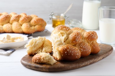 Photo of Homemade braided bread with sesame seeds on white wooden table. Traditional challah