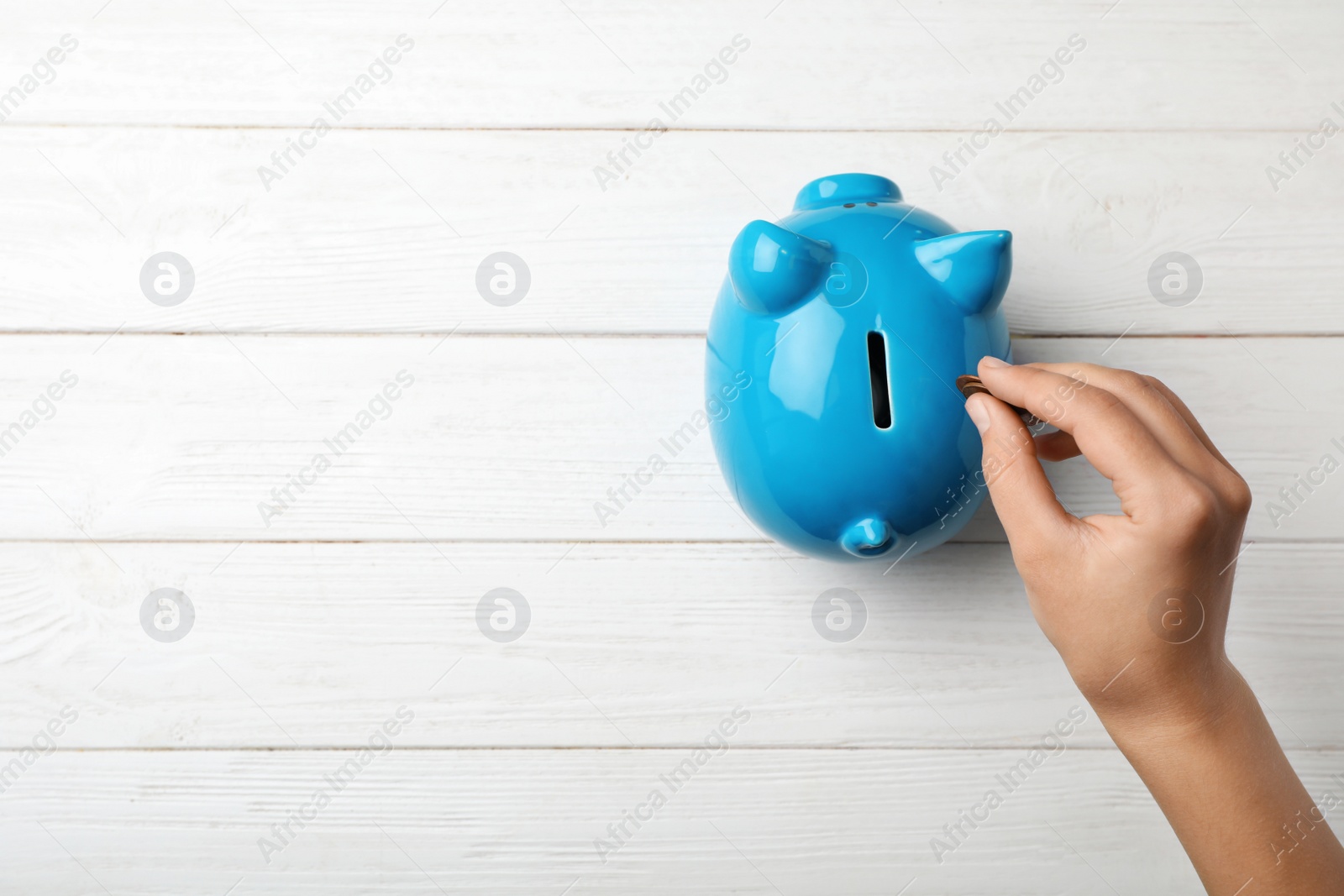 Photo of Woman putting coin into piggy bank on wooden table, top view with space for text