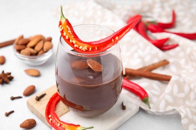 Photo of Glass of hot chocolate with chili pepper and almonds on white table