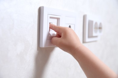 Photo of Little child playing with electrical socket indoors, closeup. Dangerous situation