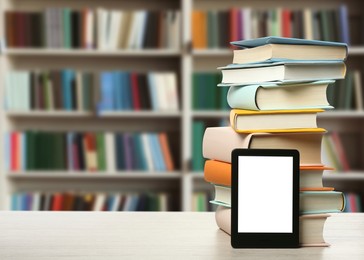 Stack of hardcover books and modern e-book on wooden table in library. Space for text