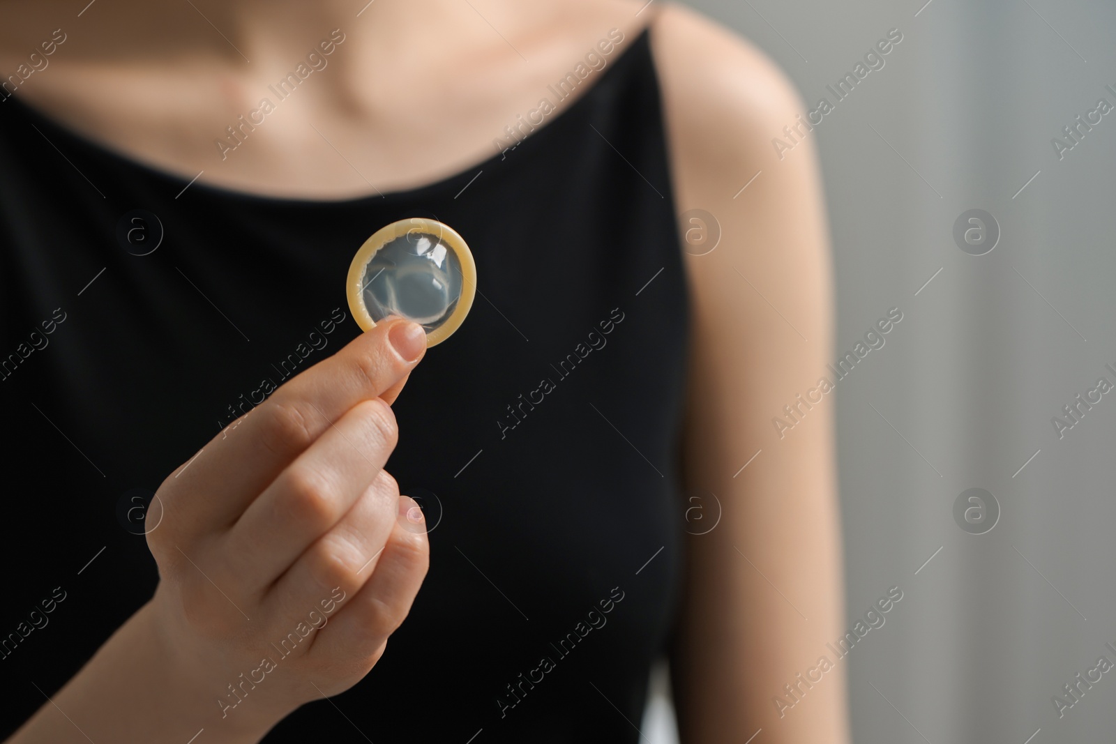 Photo of Woman holding unpacked condom on blurred background, closeup. Safe sex