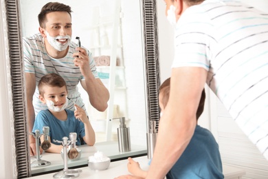 Photo of Dad shaving and little son imitating him in bathroom