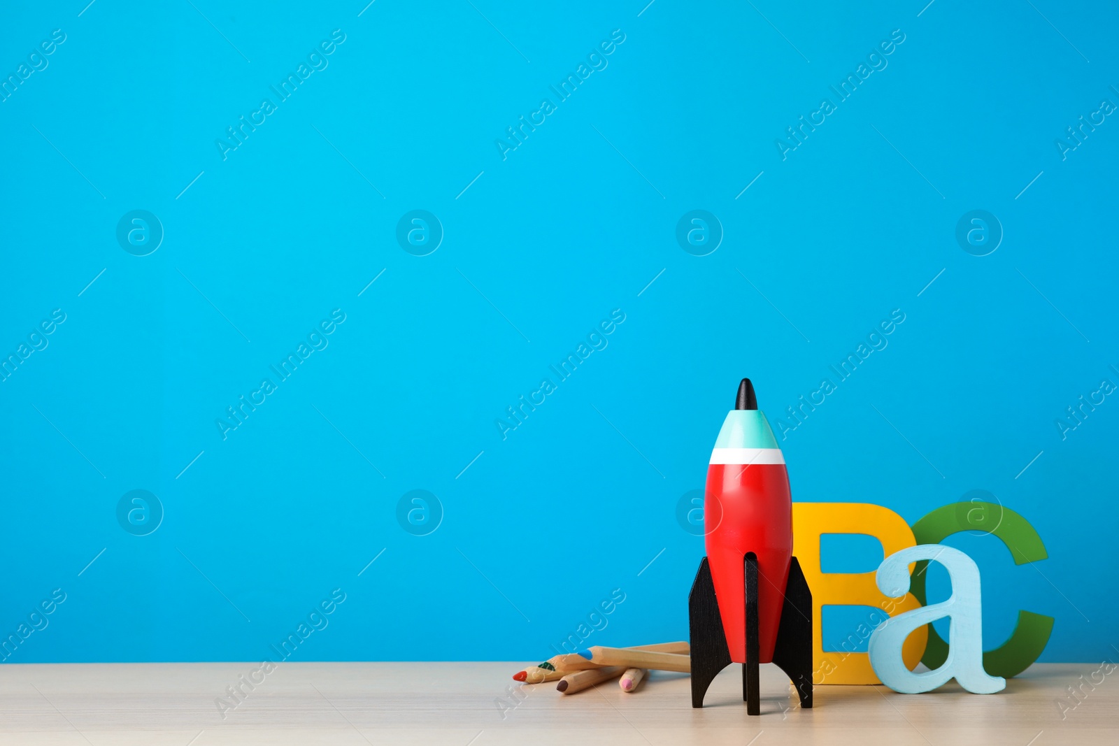 Photo of Bright toy rocket and school supplies on wooden desk. Space for text