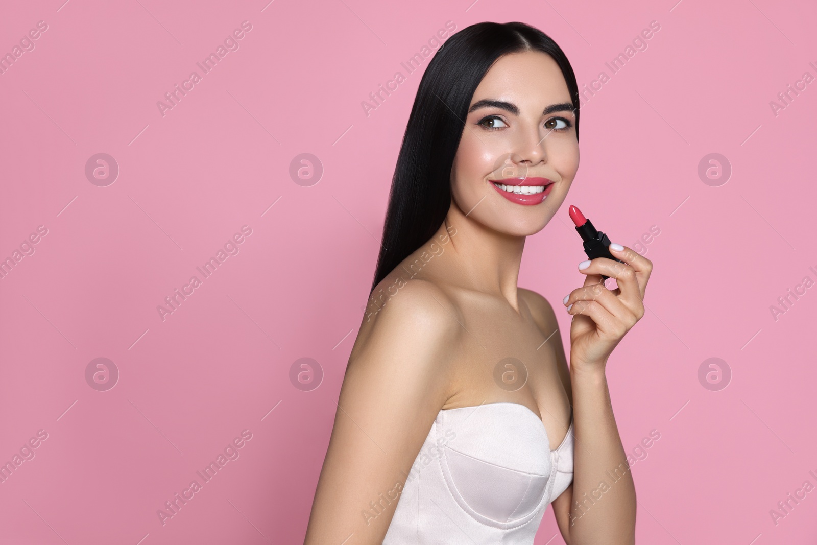 Image of Young woman with beautiful makeup holding glossy lipstick on pink background, space for text