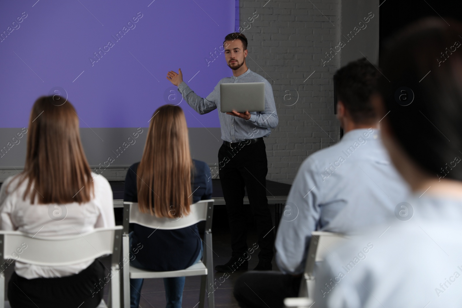 Photo of Male business trainer with laptop giving lecture in conference room with projection screen