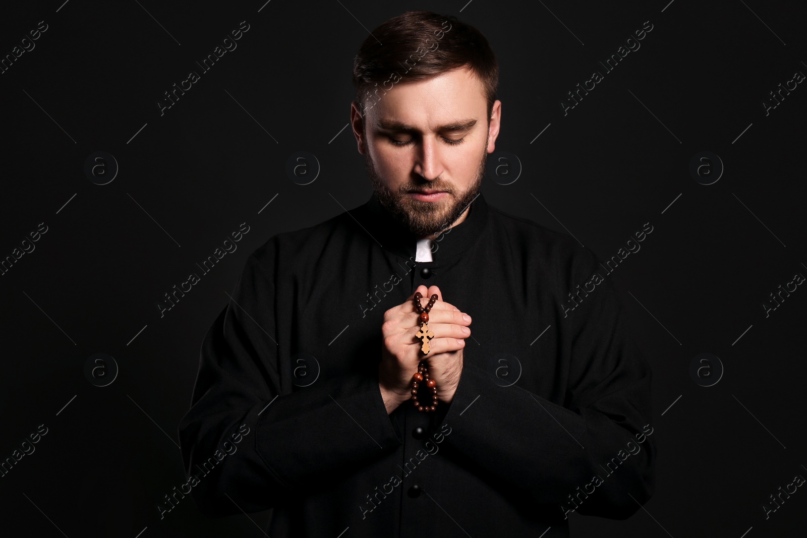 Photo of Priest with rosary beads praying on black background