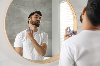 Photo of Man spraying luxury perfume near mirror indoors