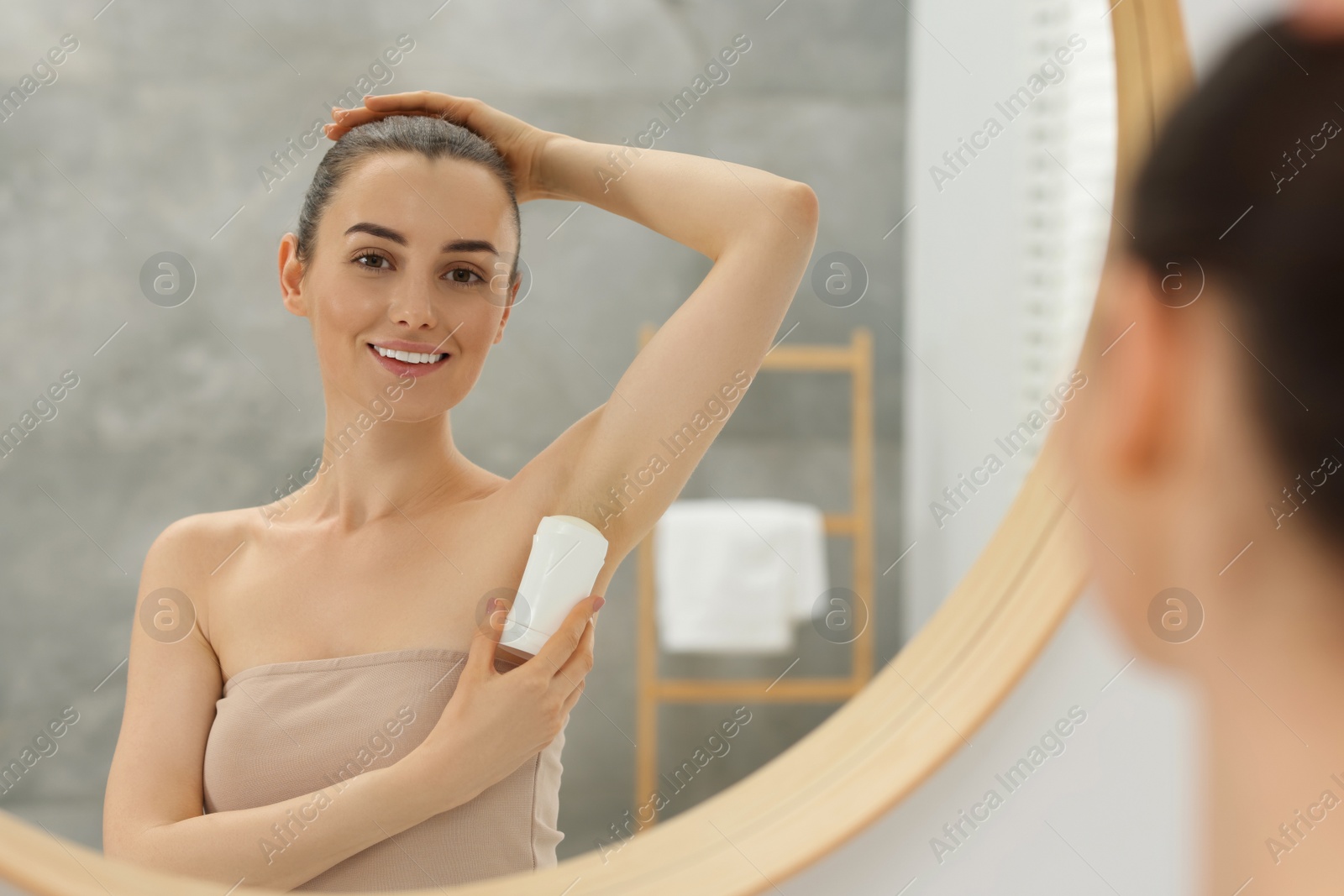 Photo of Beautiful woman applying deodorant near mirror in bathroom