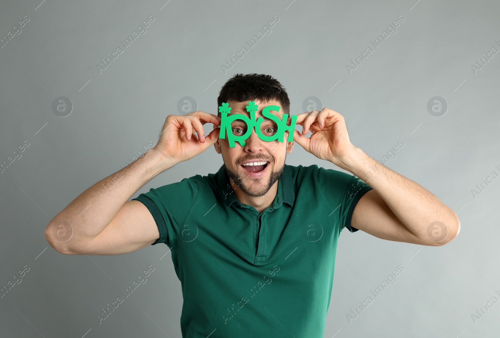Photo of Happy man in green shirt and party glasses on light grey background. St Patrick's Day celebration