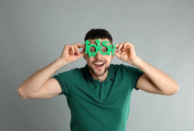 Happy man in green shirt and party glasses on light grey background. St Patrick's Day celebration