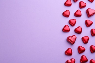 Heart shaped chocolate candies in red foil on violet background, flat lay. Space for text