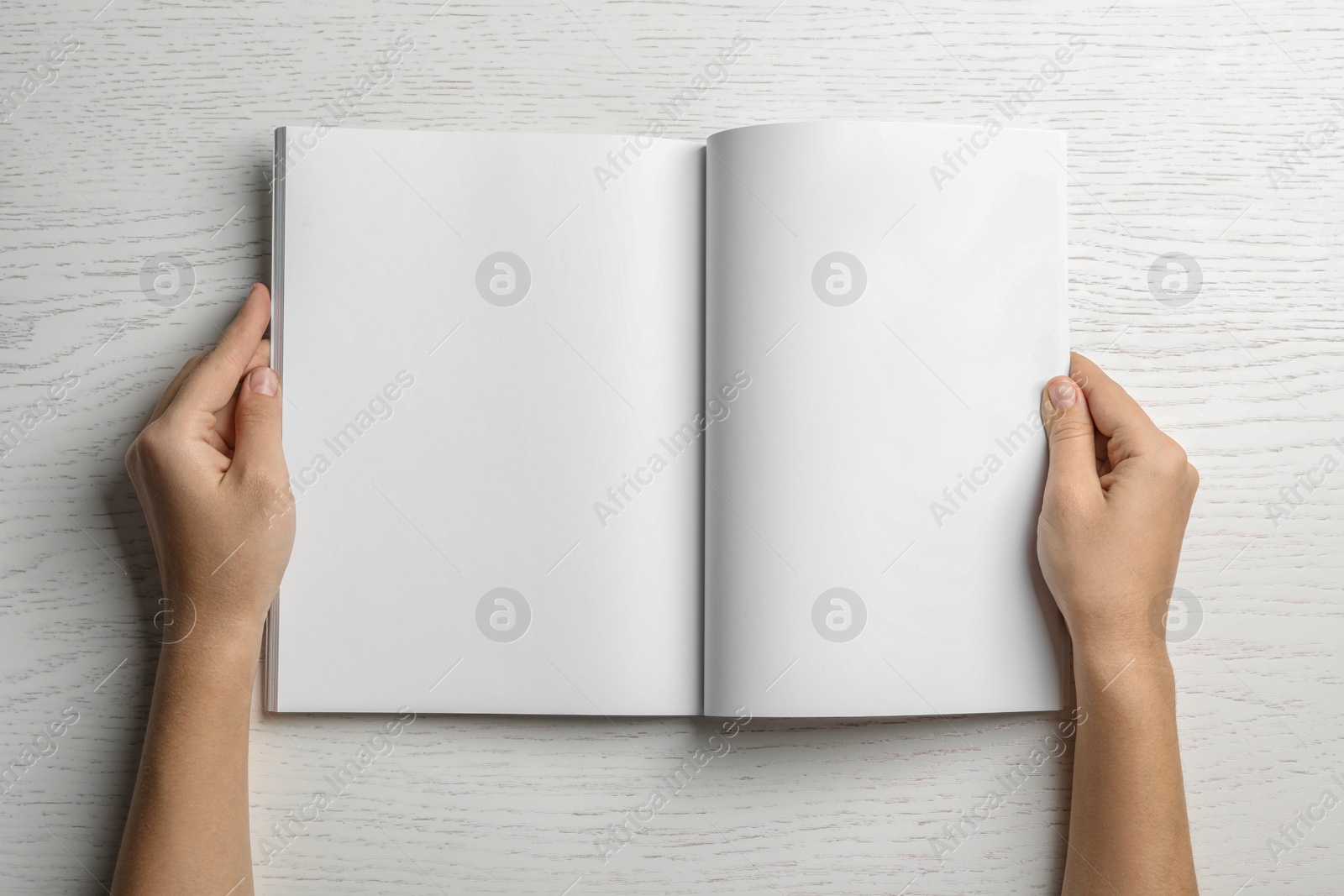 Photo of Woman holding brochure with blank pages on wooden background, top view. Mock up for design