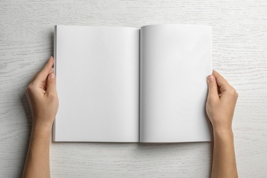 Photo of Woman holding brochure with blank pages on wooden background, top view. Mock up for design