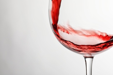 Photo of Pouring red wine into glass on light background, closeup