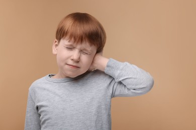 Photo of Hearing problem. Little boy suffering from ear pain on pale brown background, space for text