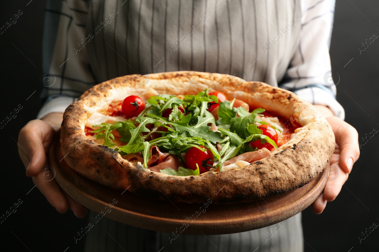 Photo of Woman holding tasty pizza with meat and arugula on black background, closeup