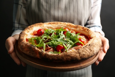 Photo of Woman holding tasty pizza with meat and arugula on black background, closeup