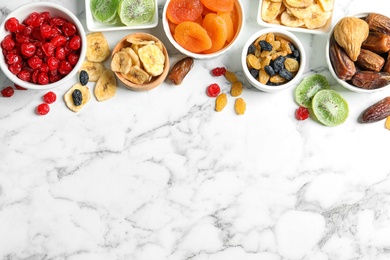 Photo of Bowls of different dried fruits on marble background, top view with space for text. Healthy lifestyle