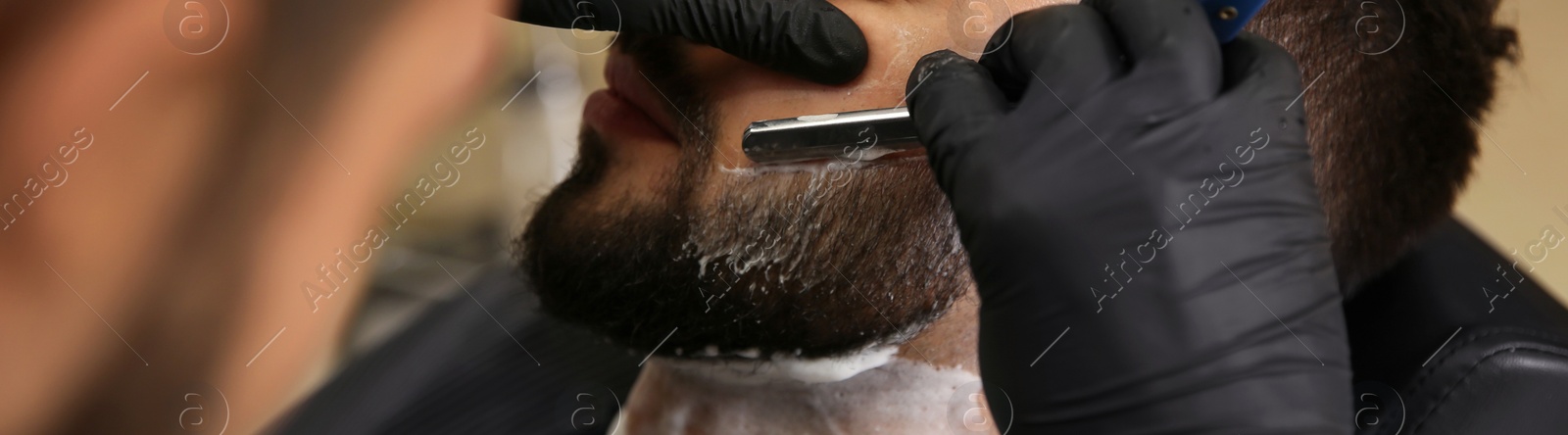 Image of Professional hairdresser shaving client with straight razor in barbershop, closeup. Banner design