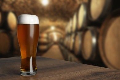 Image of Glass with fresh beer on wooden table in cellar, space for text