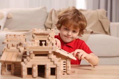 Photo of Cute little boy playing with wooden castle at table in room. Child's toy