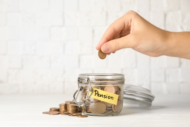 Woman putting coin in glass jar with label "PENSION" on table, closeup. Space for text