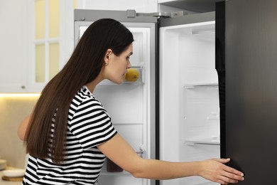 Photo of Young woman near empty refrigerator in kitchen