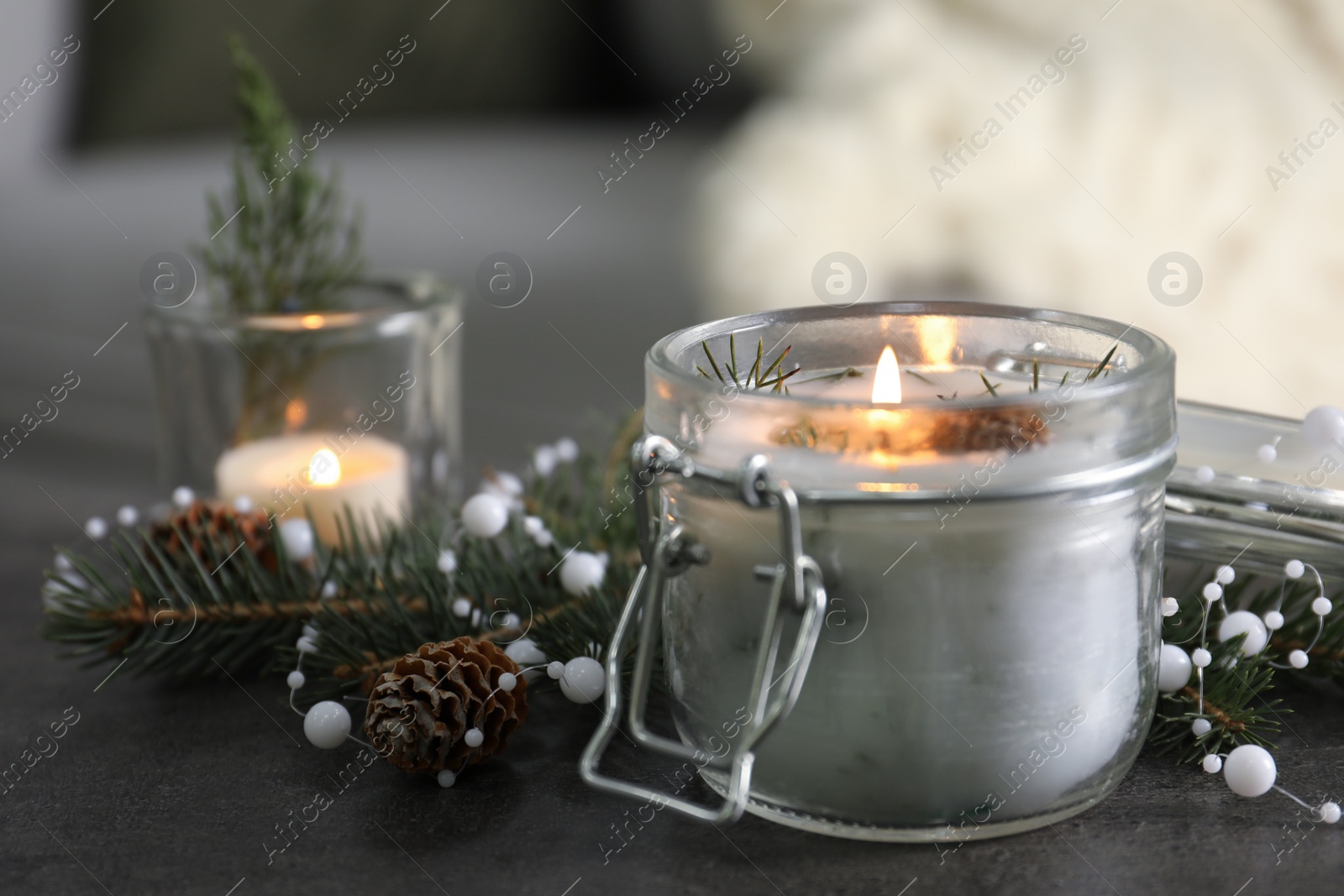 Photo of Burning scented conifer candle and Christmas decor on grey table indoors
