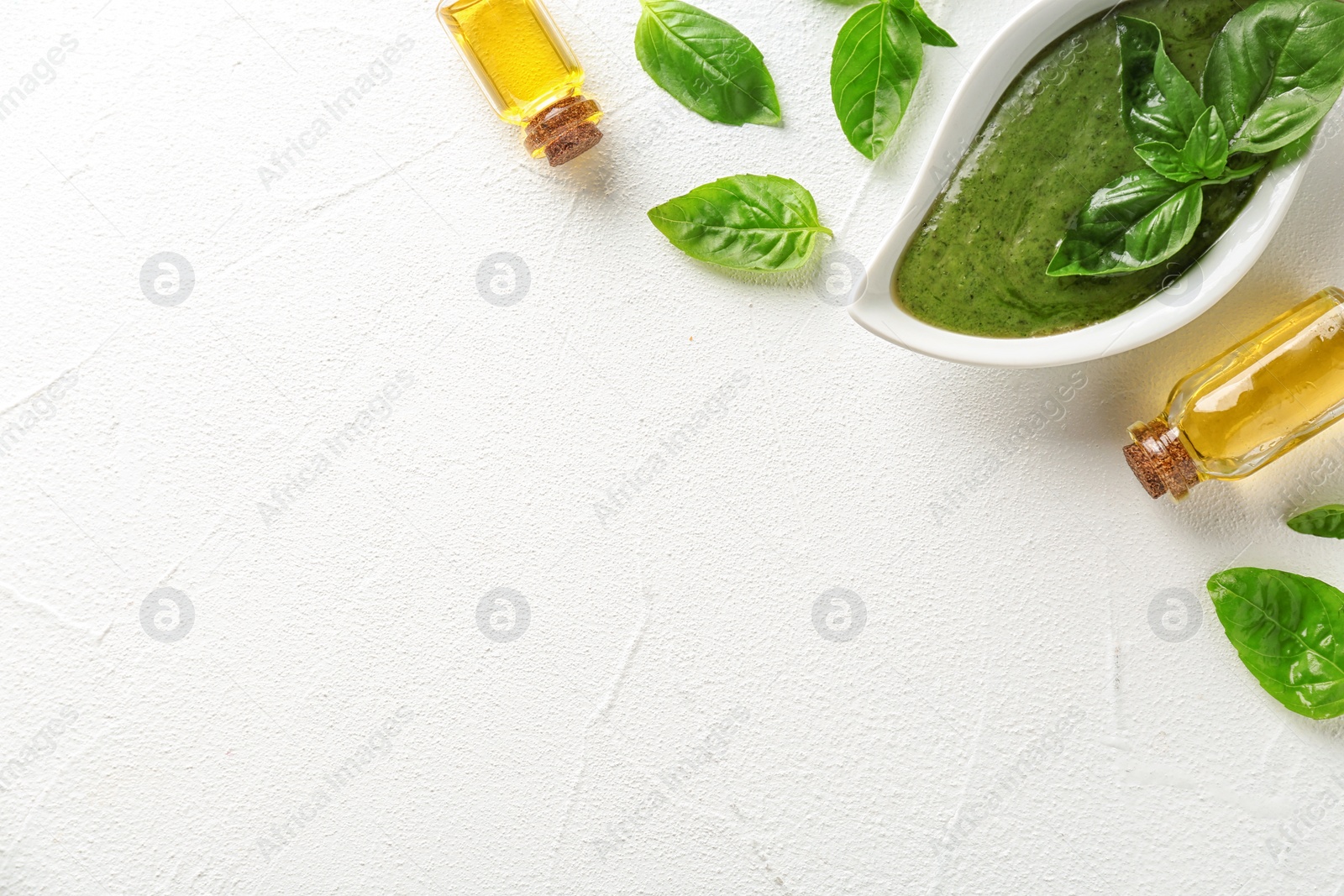 Photo of Sauce in gravy boat, basil oil and leaves on white table, top view with space for text