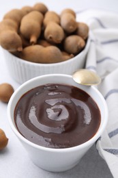Photo of Bowl of tamarind sauce, spoon and fresh pods on light table
