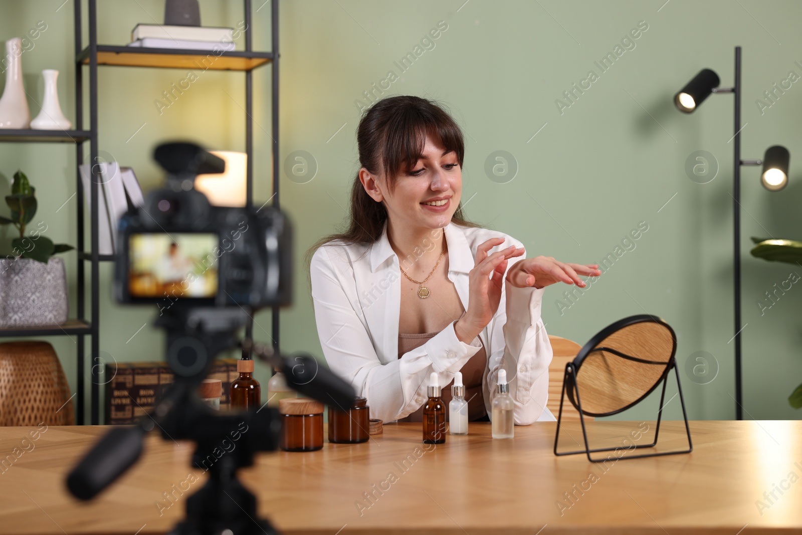 Photo of Smiling beauty blogger recording video while testing cosmetic products at home
