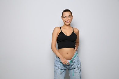 Photo of Slim woman in oversized jeans with measuring tape on light background. Weight loss