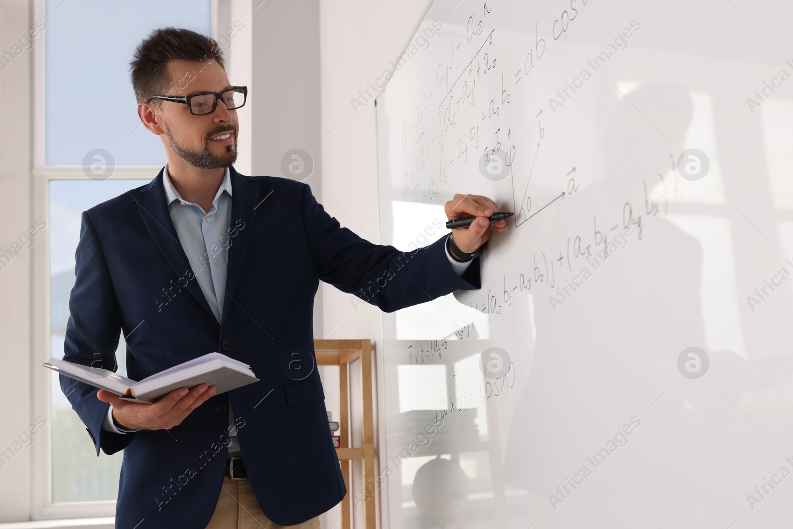 Photo of Happy teacher with book explaining mathematics at whiteboard in classroom