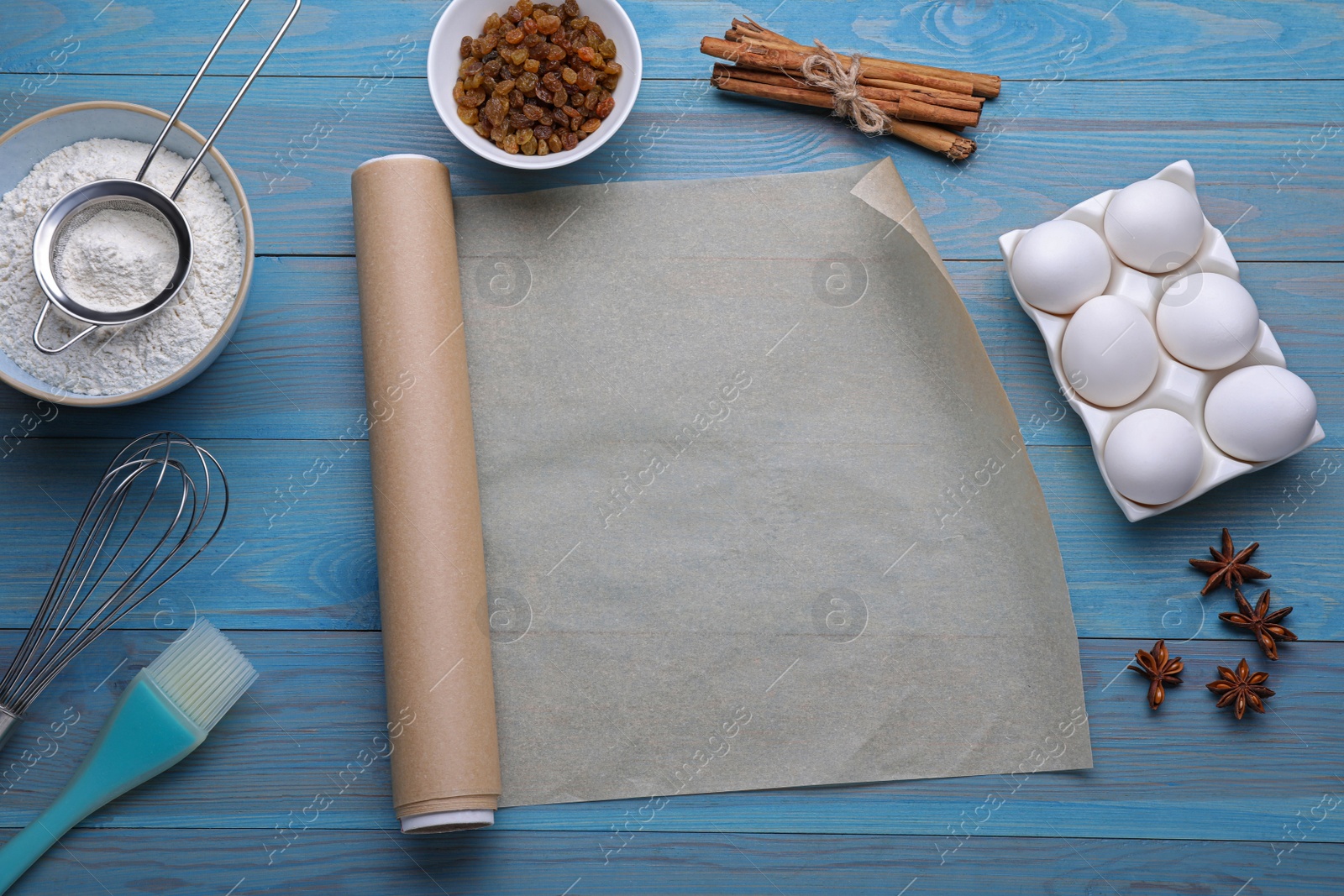 Photo of Baking parchment paper, kitchen tools and different ingredients on light blue wooden table, flat lay. Space for text