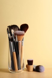Photo of Set of professional makeup brushes on wooden table against beige background